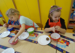 Dwoje dzieci formuje kule czekoladowe z ciasta. Jedna dziewczynka obtacza kulę w wiórkach kokosowych.